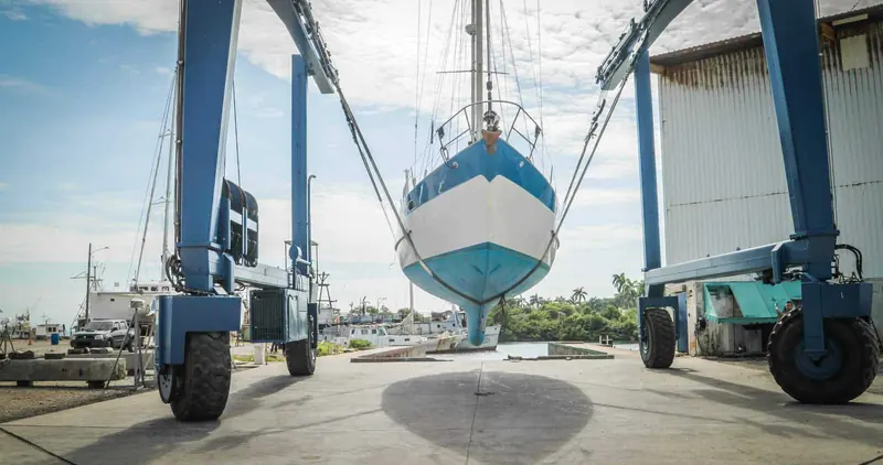 A sailboat suspended in the marina's own 100-ton travel lift, wide enough for a 28 ft beam, in the boatyard behind the docks.