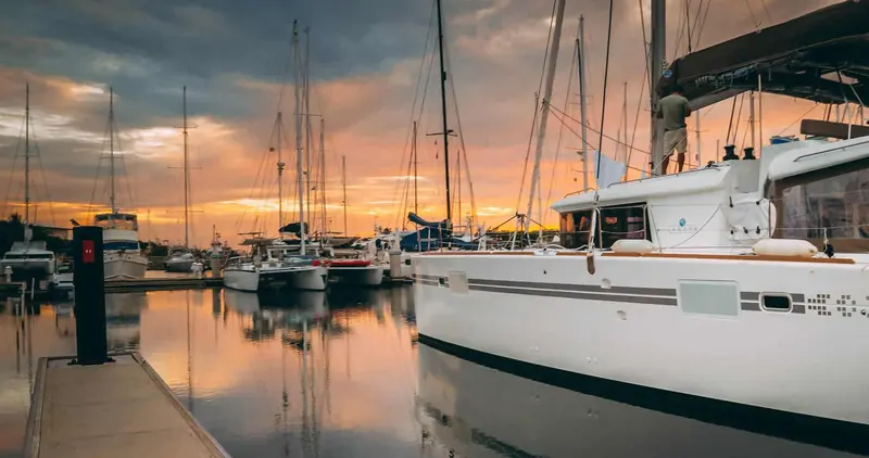 Catamarans and monohulls rafted along a finger pontoon as the sun sets over the jungle shoreline of San Lorenzo Protected Area.
