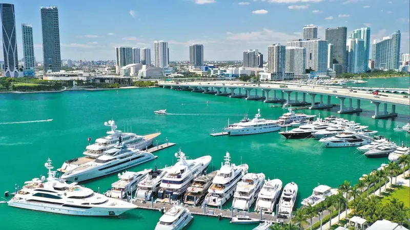 Superyachts three-deep on the pontoons at Yacht Haven Grande, with the MacArthur Causeway bridge carrying traffic into downtown Miami behind them.