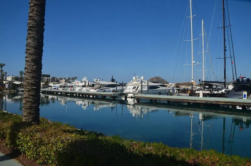 Motor yachts lie berthed in line along the main pontoon at Yalikavak, two tall sailing rigs on the outer berths and the basin dead flat behind the breakwater.