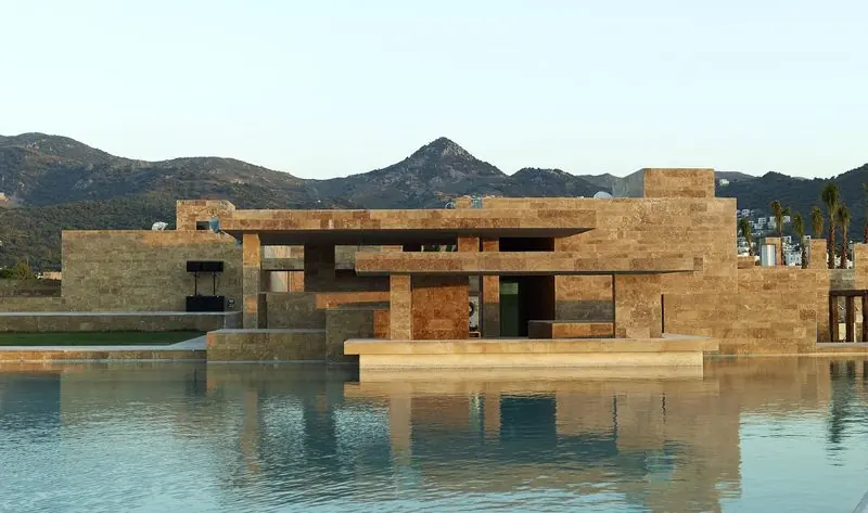 Ashore, the marina's travertine clubhouse steps down to a still water terrace, with the bare hills behind Yalikavak holding the last of the light.