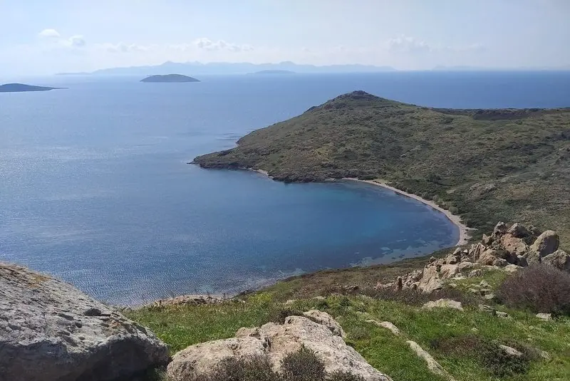 Bare green headlands wrap a deep clear bay on the Yalikavak peninsula, with further islands lying hazy on the horizon beyond.