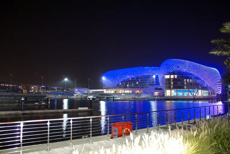 The Yas Viceroy's LED-lit bridge spans the water above the marina at night, yachts moored along the quay below.