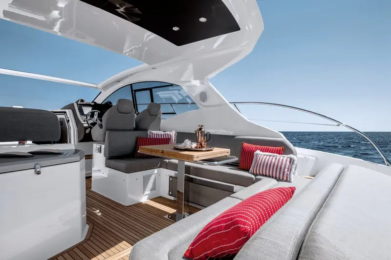 Helm and cockpit dining share the same shaded bay under the hardtop, with the wheel angled for a clear view over the bow.