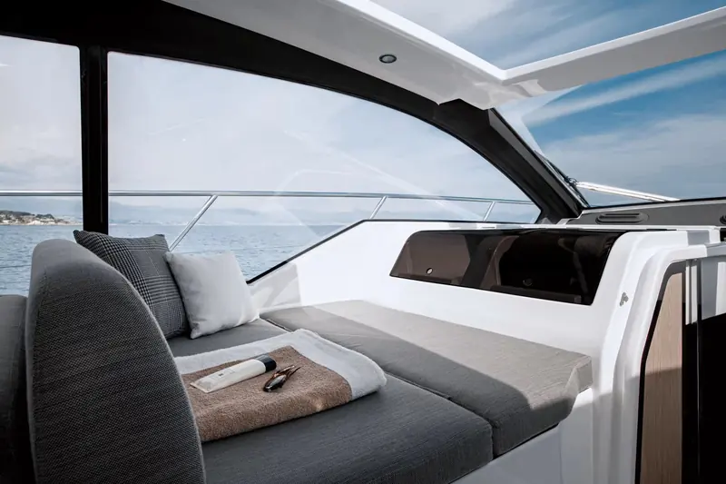 The cockpit lounge under the hardtop, open on three sides, with the coastline visible through the side glazing rather than boxed in by a flybridge overhead.