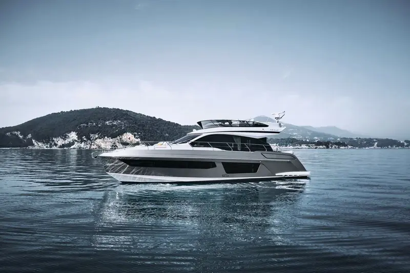 Azimut Fly 53 at anchor off a wooded headland, the two-deck flybridge profile and reverse bow visible in profile.