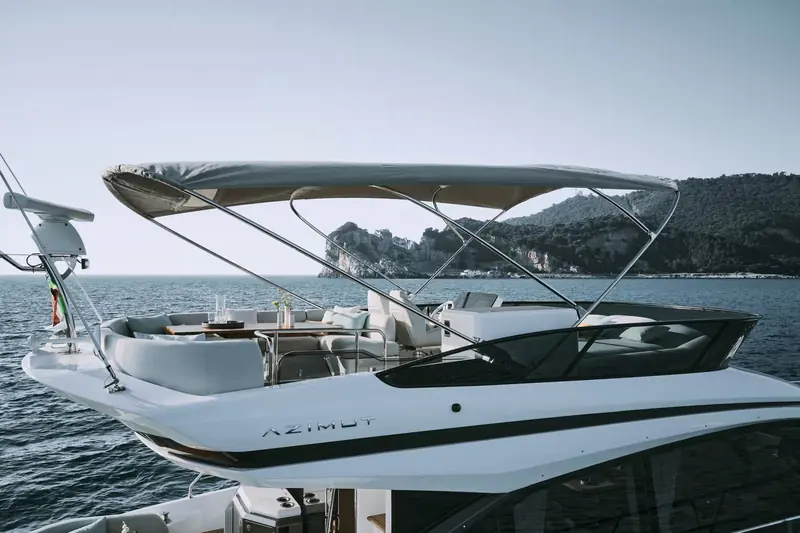 The flybridge shaded under its bimini, with forward-facing lounge seating ahead of the upper helm station.