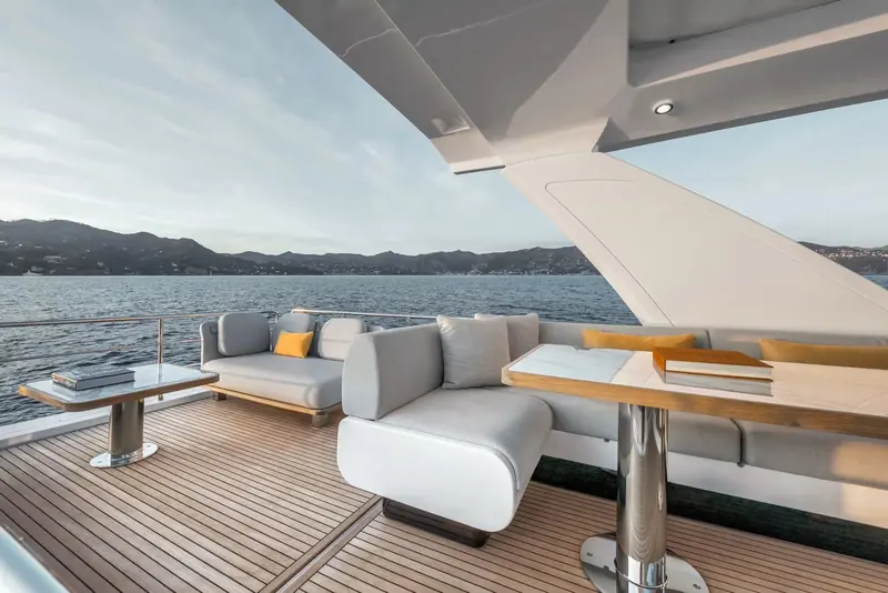 Flybridge seating set around a low table, shaded by the hardtop with the coastal hills behind.