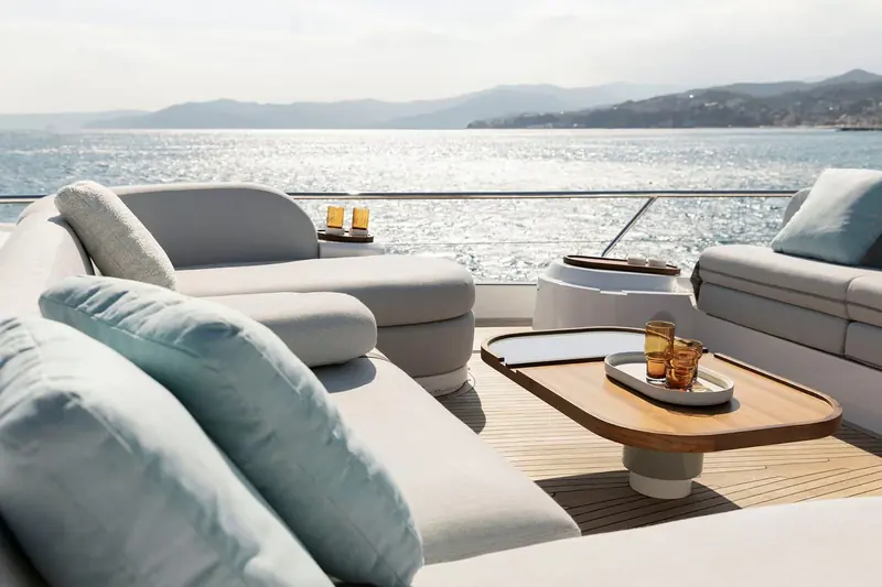 A second flybridge angle looking aft over a wooded shoreline, cushions squared and shaded seating built around a low central table.