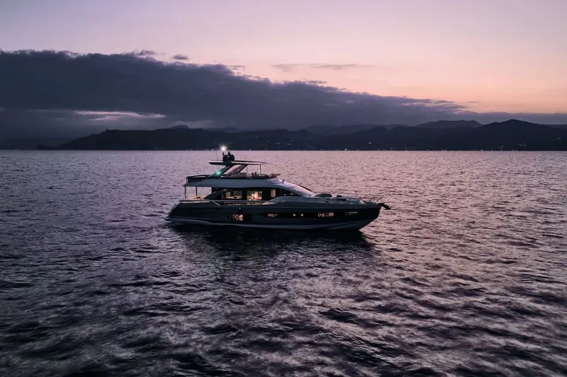 At anchor at dusk, hull lights picking out the full-beam glazing that runs almost the length of the main deck saloon.