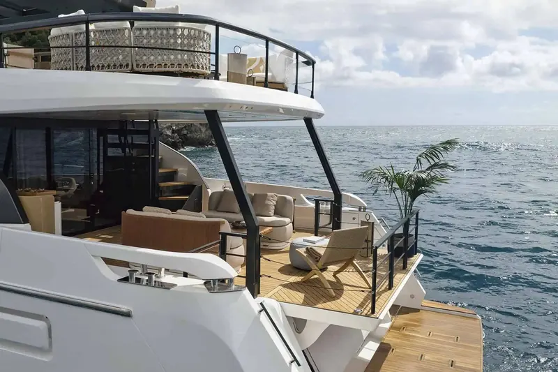 Looking aft from the flybridge stairs toward the swim platform, with the tender and beach-club furniture visible on the transom deck below.