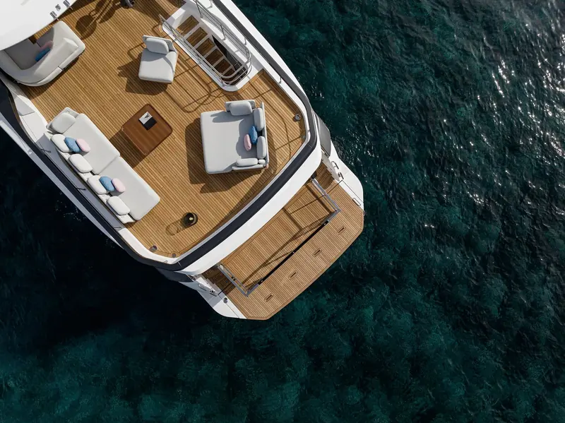 The transom beach club platform lowered to the water, teak underfoot and twin loungers either side of the swim step, framed by a wake curling away from the hull.