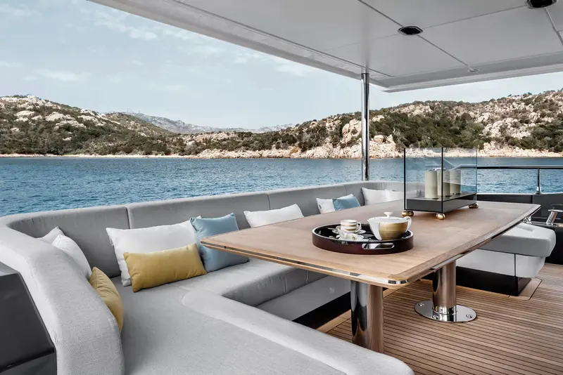 The aft cockpit dining table, set beneath an open rail with the coastline in full view rather than screened by solid bulwarks.