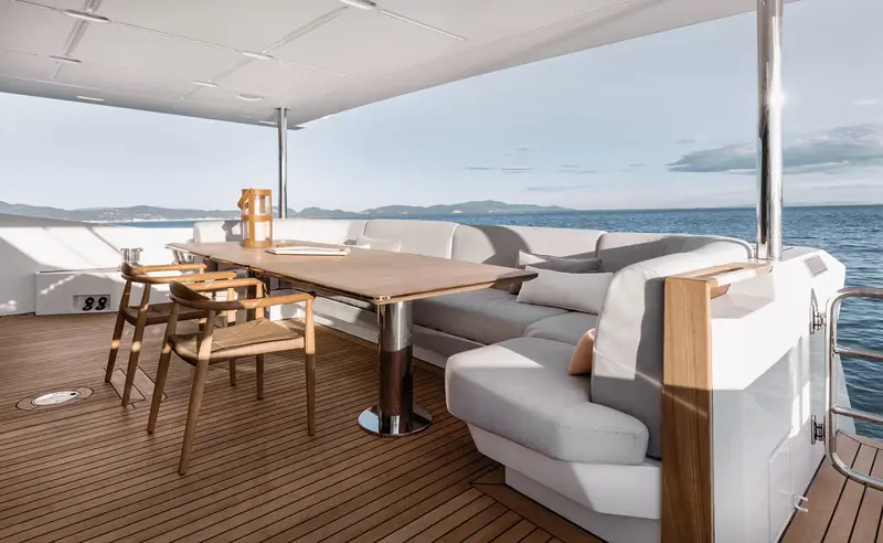 The aft cockpit dining table under the hardtop, with teak decking and a fixed lounge that seats the whole party without moving furniture.