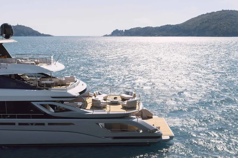 Seen from astern arriving at a headland near Portofino, showing the flybridge sunpad, the swim platform and the tender garage doors closed flush into the transom.