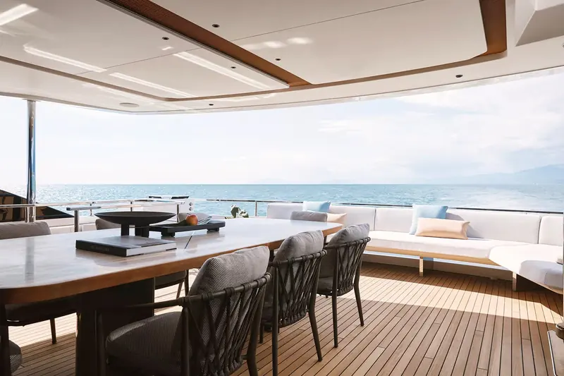 The upper-deck aft dining table set for eight under the hardtop, open on three sides to the sea with no glazing between the diners and the view.