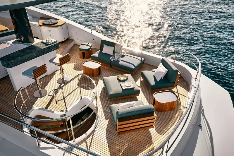 The flybridge wet bar and aft lounge, with the spiral stair down to the cockpit on the left - the sunpad and seating here are as much the point of the boat as the range is.