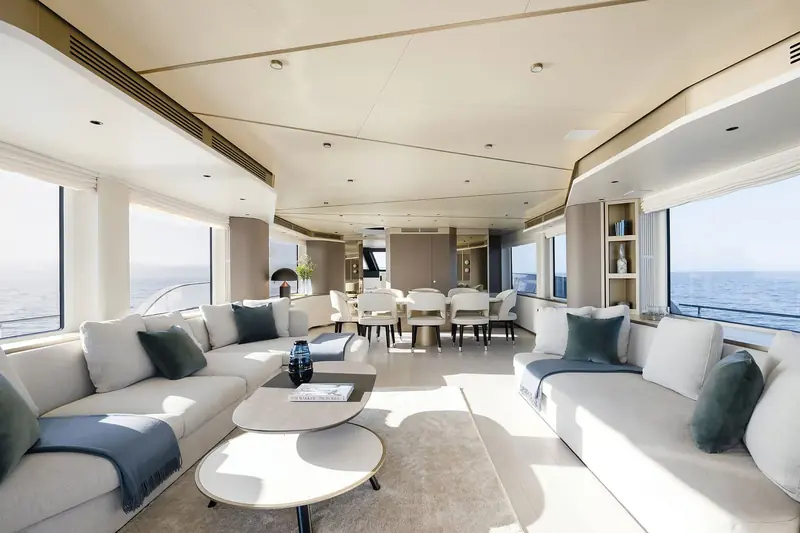 The main-deck saloon and dining table, with full-height glazing on both sides keeping sightlines to the water from every seat, not just the window rows.