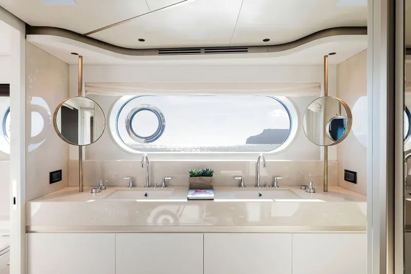 An owner's bathroom built around a single oval porthole rather than a conventional window - a detail that reads as a proper yacht rather than an apartment afloat.