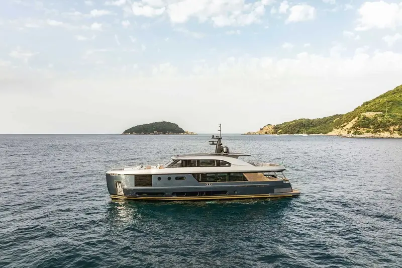 Broadside past a small island, showing the semi-displacement hull's deeper forefoot compared with a planing flybridge yacht.