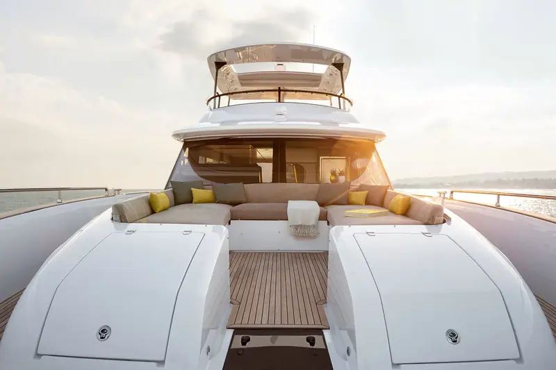 The flybridge aft lounge, teak-topped table laid with yellow accent cushions and an unbroken rail view back over the wake.