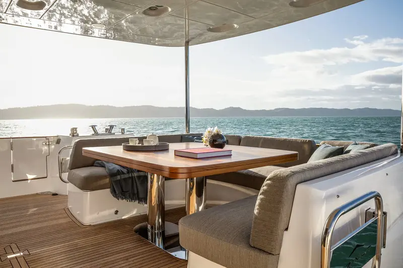 Aft cockpit dining under the hardtop overhang, a coffee-table book left open on the table and stainless stanchions polished to a mirror finish.