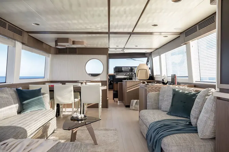 The main-deck saloon looking aft, low L-shaped seating and a teak sole that carries the same wood tone through from the galley.