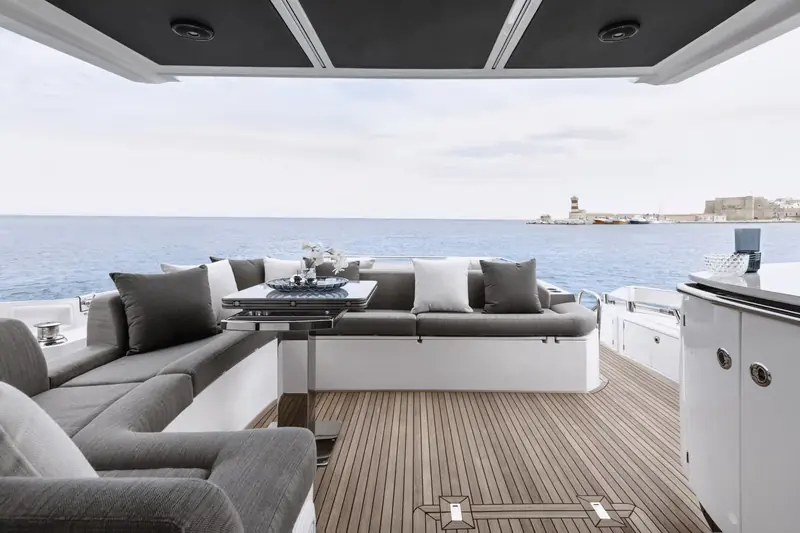 The aft cockpit lounge, an L-shaped sofa and table set against open transom rail, with a wet bar unit built into the port side.