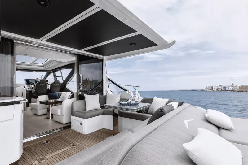 Looking forward through the cockpit into the glazed salon, showing the low-profile helm seating and the openness between indoor and outdoor space that the coupe layout is built around.