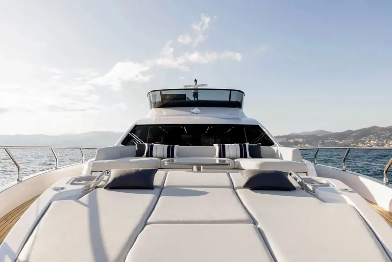 The foredeck sunpad seen from directly ahead, framed by the stainless bow rail with the coastline running along the horizon.