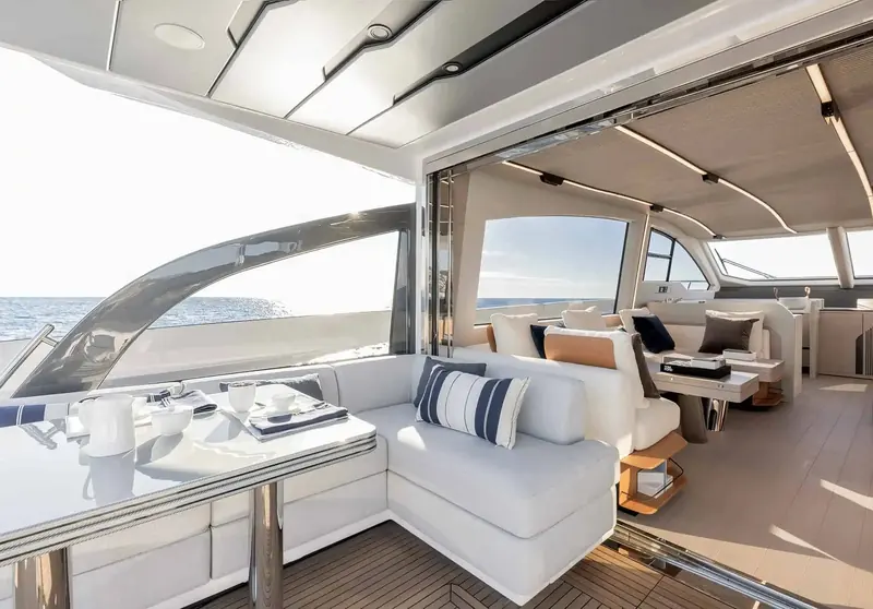 The flybridge lounge and dining table under the retractable hardtop, set up for entertaining with cushions and a full place setting.