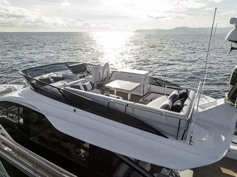 An elevated view down onto the flybridge at sunset, with the twin helm seats, u-shaped lounge and dinette table laid out around a wet bar unit.