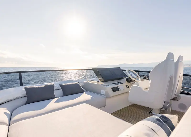 The flybridge helm seat and wheel in bright sun, showing the bolstered single helm chair and forward view over the bow.