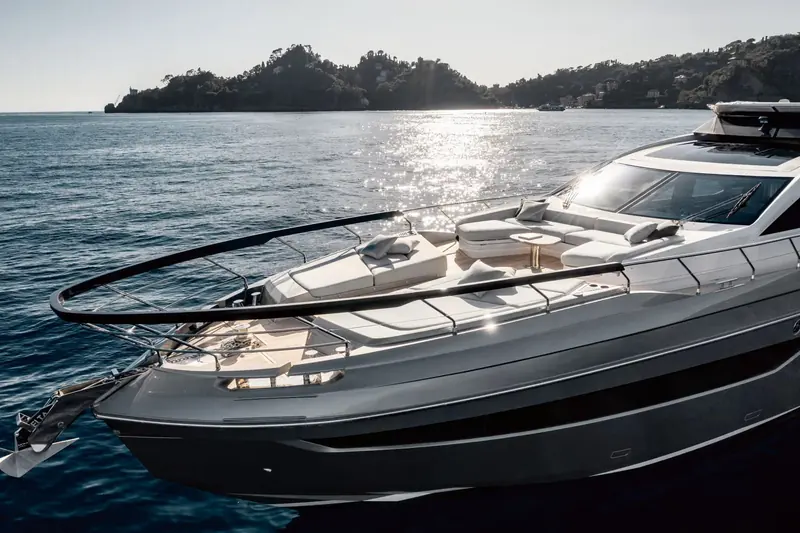 At anchor off a pine-covered headland, sun glinting off the flybridge screen - the wraparound glass that gives the sportfly helm shelter without closing it in.