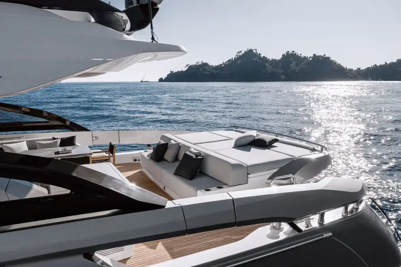 The transom sunpad and swim platform at anchor, low sun catching the water off a wooded point astern.