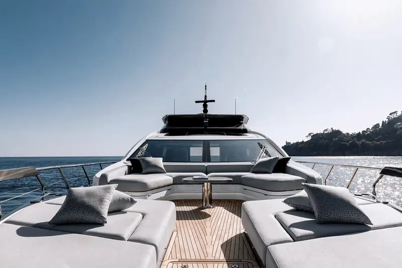 The foredeck sunpad forward of the windscreen, cushions squared away and a headland framed beyond the pulpit rail.