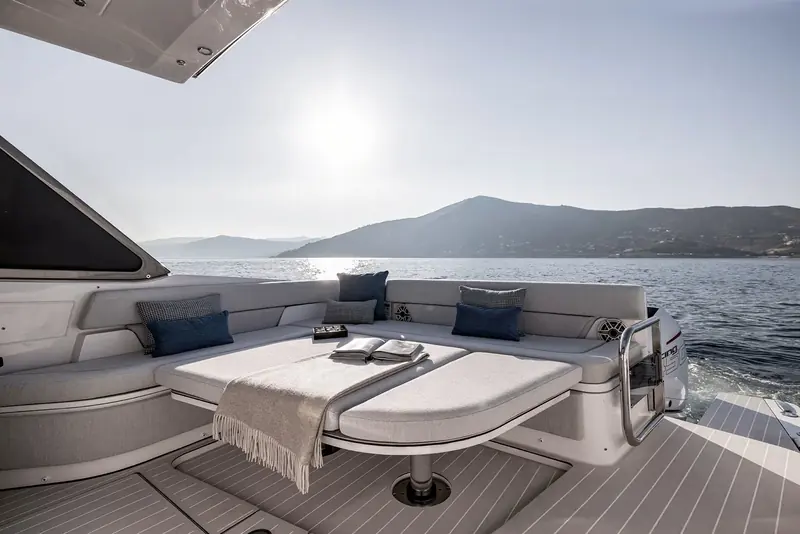The aft cockpit's convertible dinette folded down into a sunpad, with a Mercury Racing outboard cowling and open water visible over the transom.