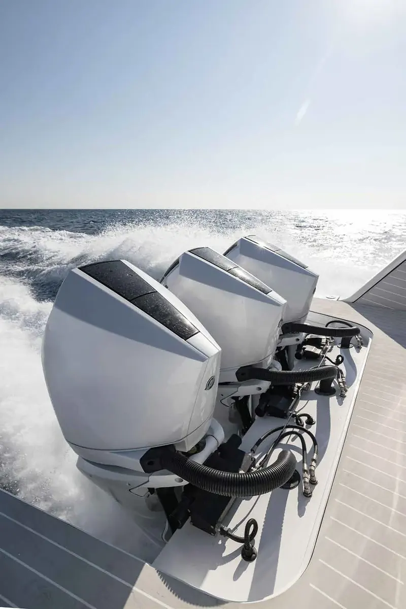 The triple Mercury outboards seen from the swim platform at speed, spray breaking either side of the transom and the rigging and steering hardware visible beneath the cowlings.