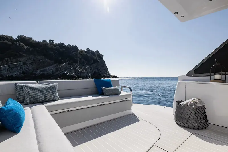 Looking out from the aft cockpit seating at anchor off Gallinara Island, with a woven storage basket on the side deck and the folded bimini frame overhead.