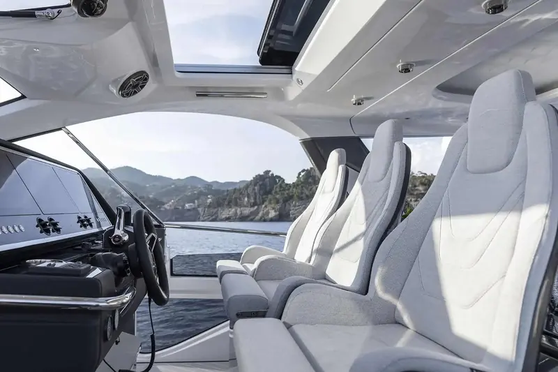 The three-across helm bench, wraparound screen open to the air rather than fully enclosed, coastline visible either side of the driver.