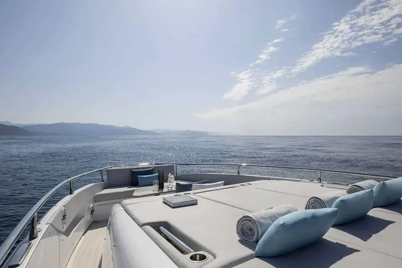 The bow sun island set for two, cushions and a book left out at anchor with the coast running along the horizon.