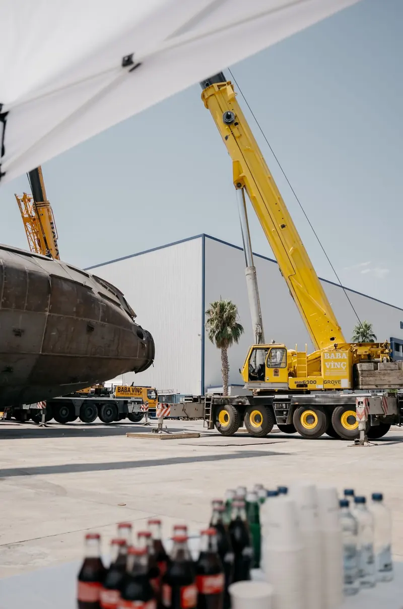 The hull suspended mid-turn, steel plating and welded seams visible before the aluminium superstructure goes on