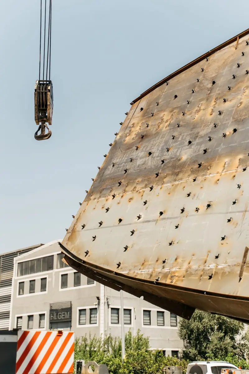 Close on the bow plating during the lift, the rivet-pattern welds of the full-displacement steel hull