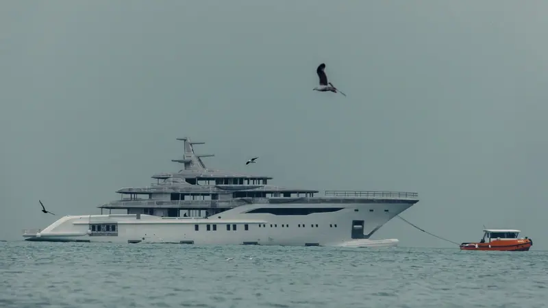 A long-lens view of the Bilgin 243 under tow, her tiered superstructure still construction-grey aluminium with no paint or glazing yet applied.
