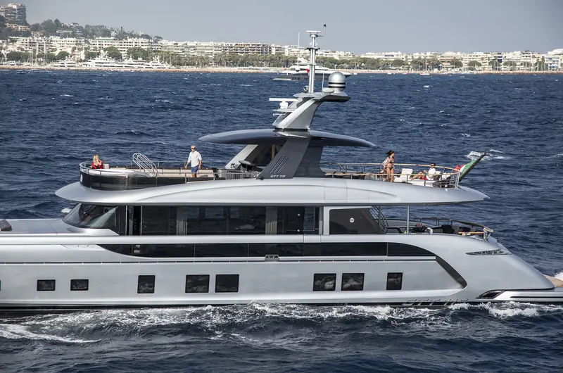 The GTT 115 and HYBRID lettering run along her topsides as she cruises past La Croisette; her sea trials logged 22 knots top speed and 17.9 knots at a 240 litre-per-hour cruise, both ahead of Dynamiq's own estimates.