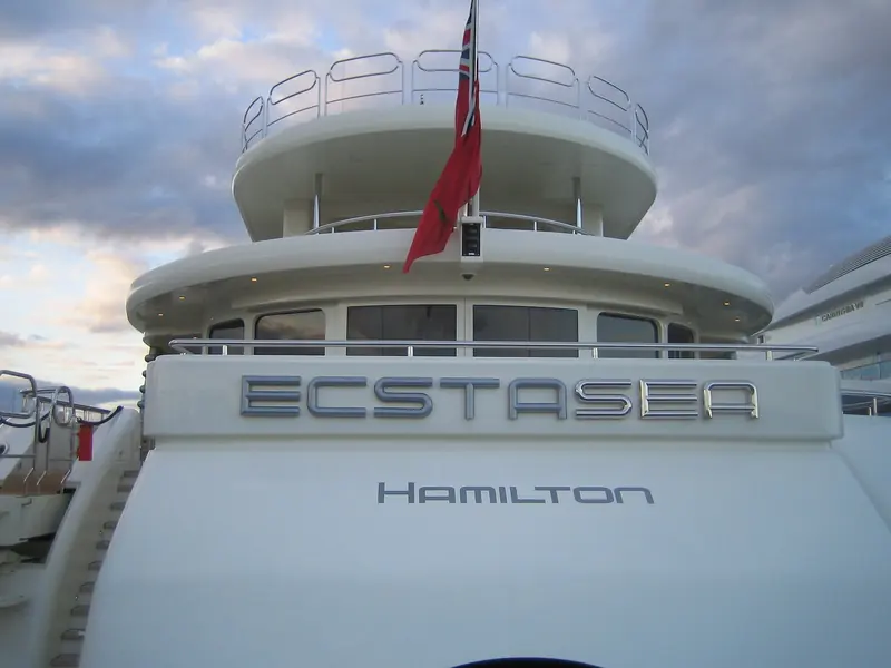 The transom under the same evening light, name and port of registry - Hamilton, Bermuda - lettered directly onto the hull rather than mounted as a separate plate.