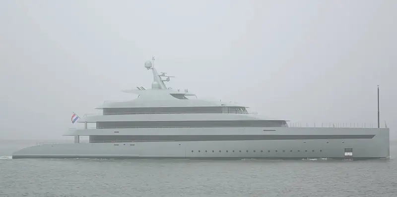 Underway in hazy conditions, hull-side glazing and the swept mast visible even at reduced visibility.