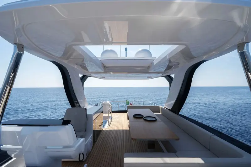 The flybridge dining table under the hardtop, helm seating to port and open sky through the sunroof overhead.