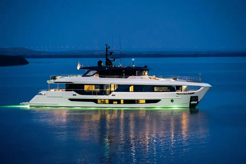 At anchor after dark, underwater lighting turning the hull's wake a pale green and every saloon window lit from inside - a genuine dusk shot, not a render.