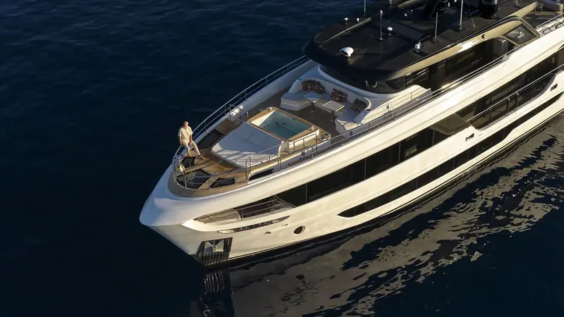 Looking down onto the foredeck terrace from above, the sunken jacuzzi and L-shaped seating laid out around it, an owner standing at the pulpit rail for scale.
